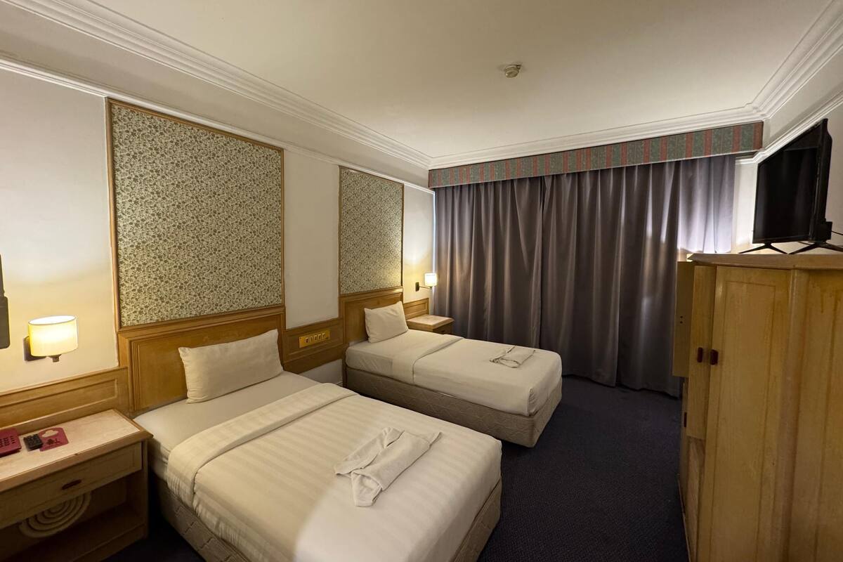 A hotel room with two beds, a television, a wardrobe, and a desk with a lamp.