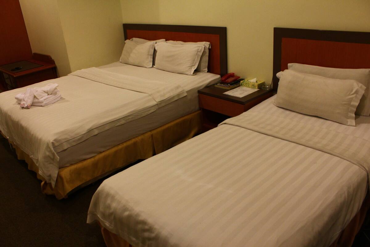 Two single beds with white linens, a bedside table with a telephone and a notepad, and a folded towel on the left bed.