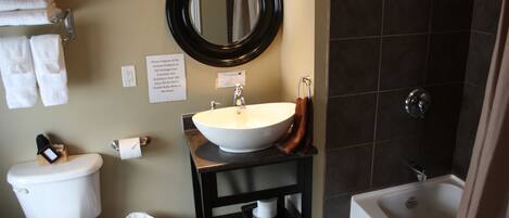 A bathroom with a toilet, sink, and bathtub. There are towels on a rack and a trash can.