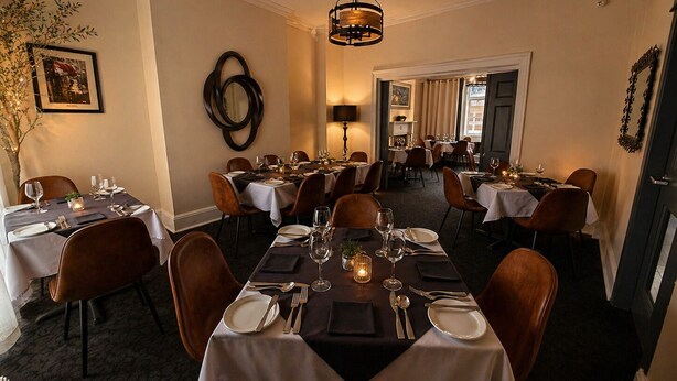 Une salle à manger élégante, avec plusieurs tables dressées pour le service, un lustre et un miroir au mur.