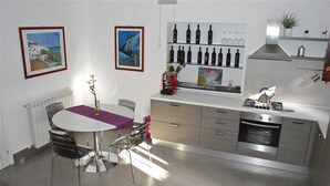 A modern kitchen with a dining table, chairs, a built-in oven, and wine bottles on shelves. - B&B Porta delle Madonie (Campofelice di Roccella)