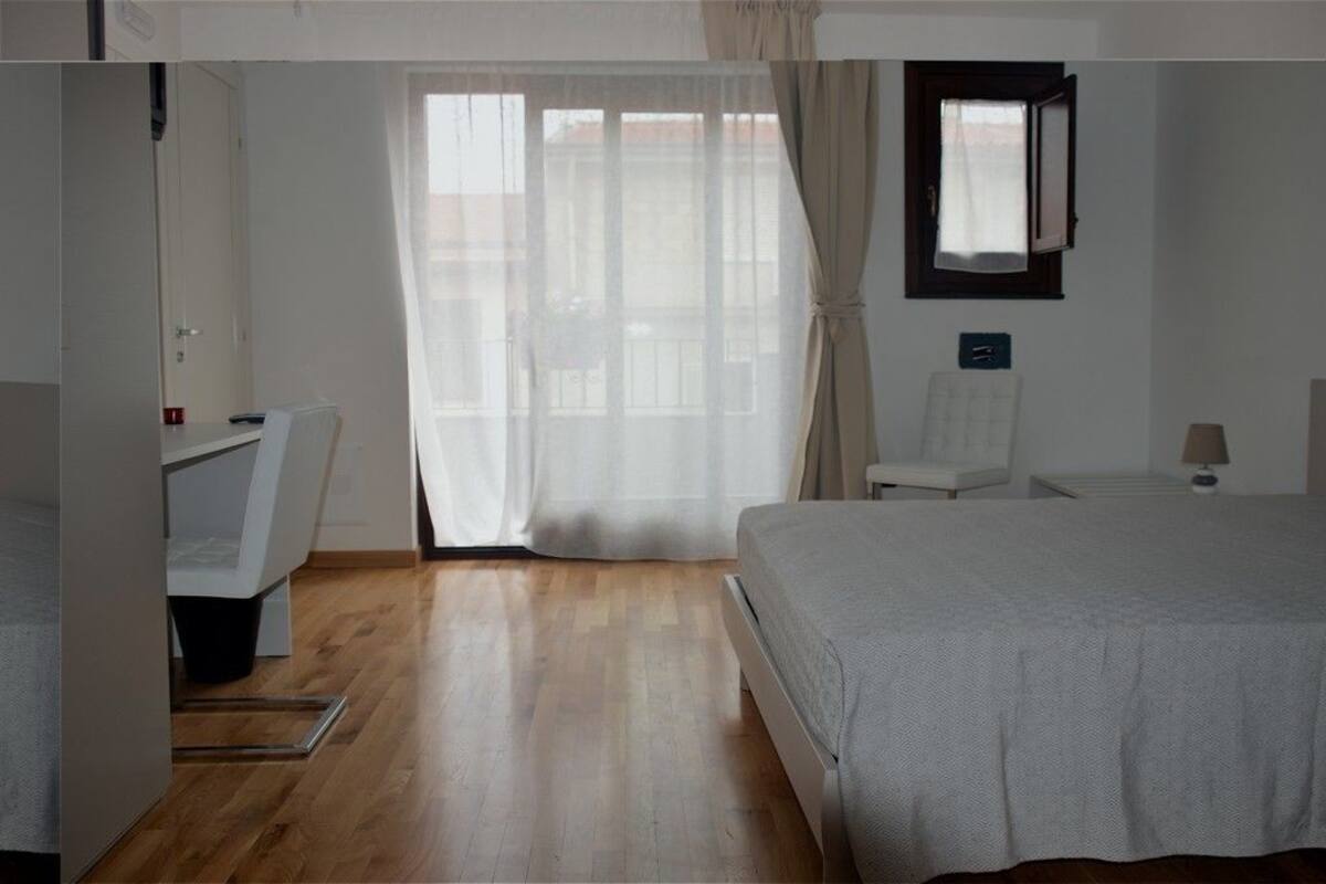 A bedroom with a bed, a desk, a chair, and a window with curtains.