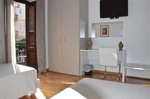 A hotel room with a bed, a desk, a chair, a TV, and a balcony with a view of the outside.