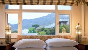 A bedroom with a bed, two bedside lamps, and a window with a view of mountains and greenery. - Rosedene Guest House (Cape Town)