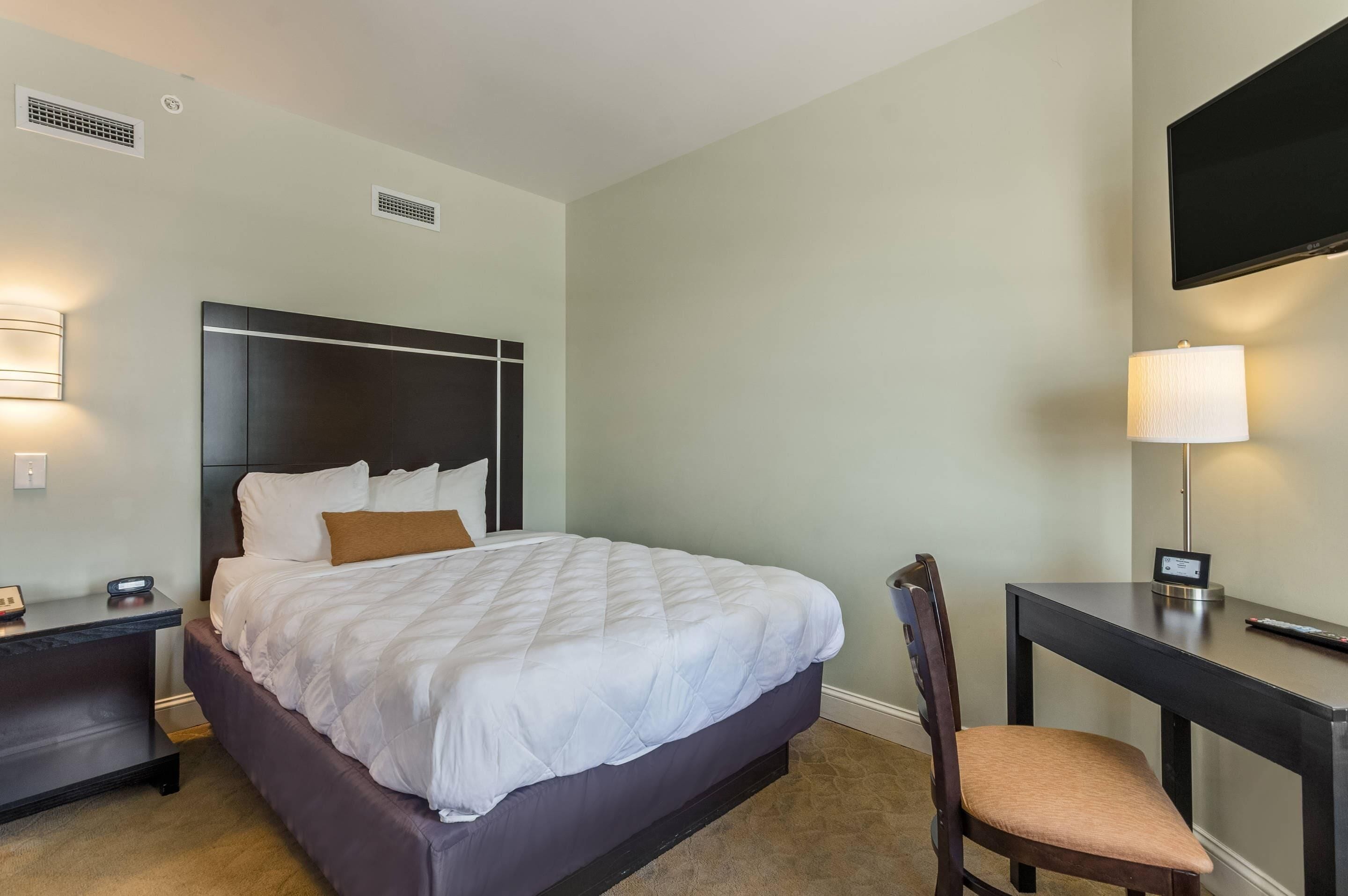 A hotel room with a bed, bedside table, lamp, chair, and a TV mounted on the wall.