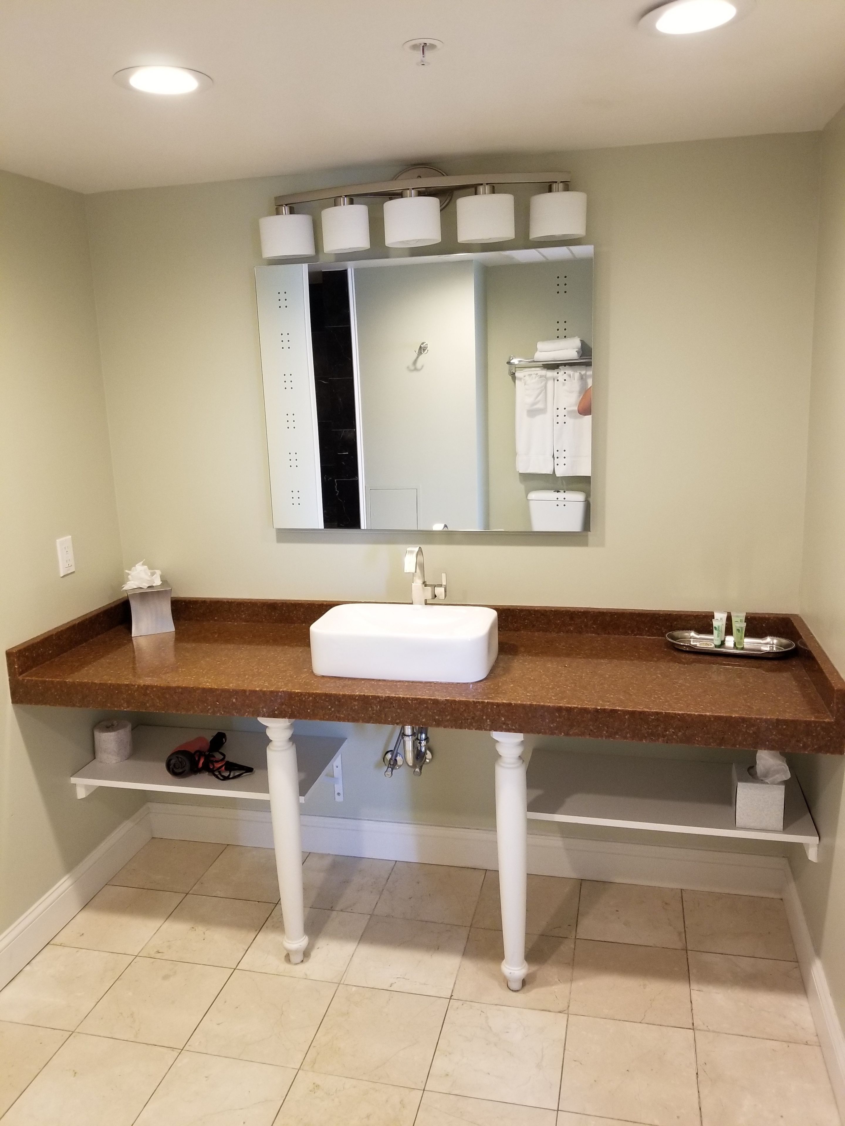 A bathroom with a white sink, brown countertop, and a large mirror above it.