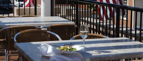 Outdoor dining tables with wicker chairs, a glass of wine, and an American flag.