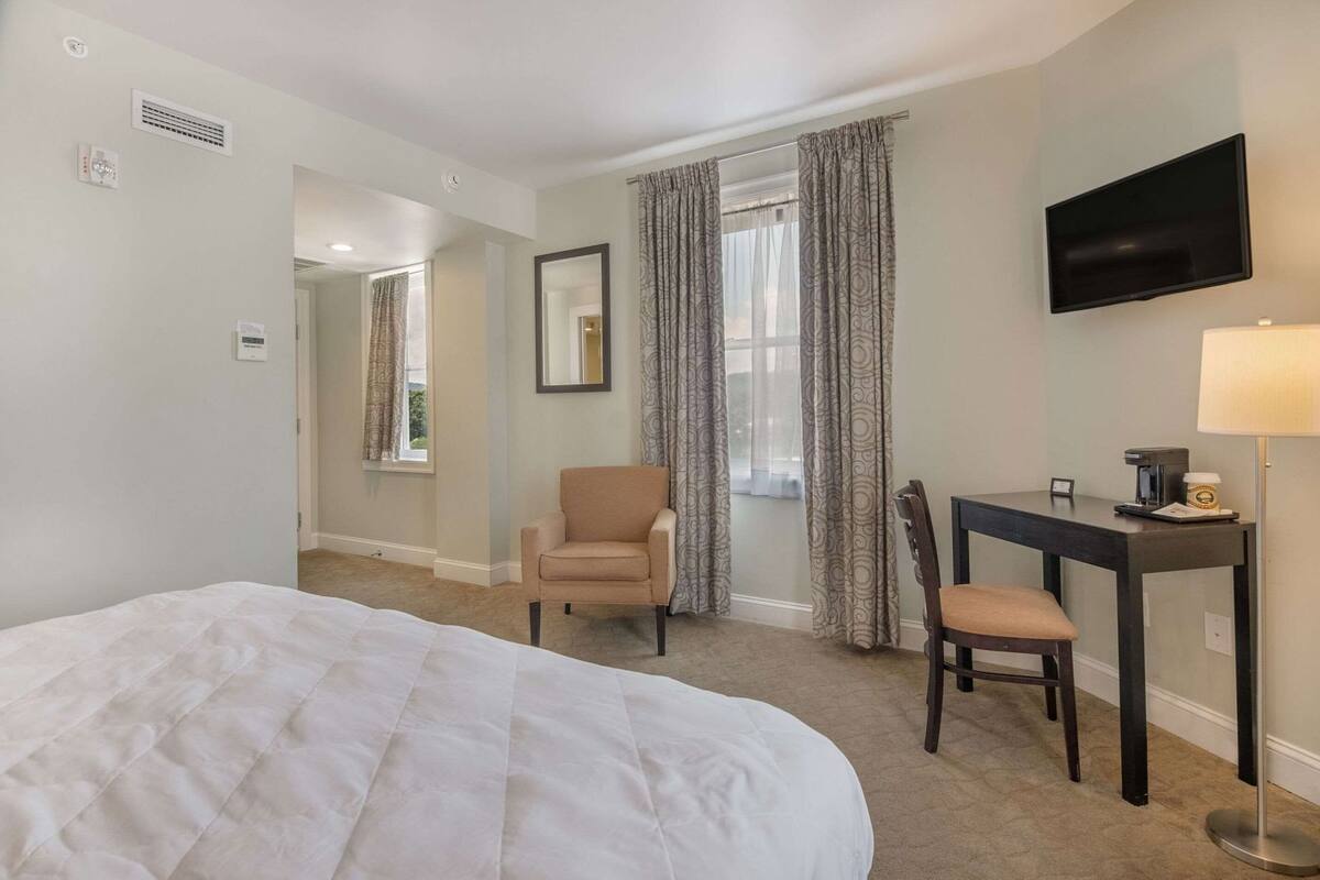 A hotel room with a bed, a desk with a chair, a TV, and a lamp.