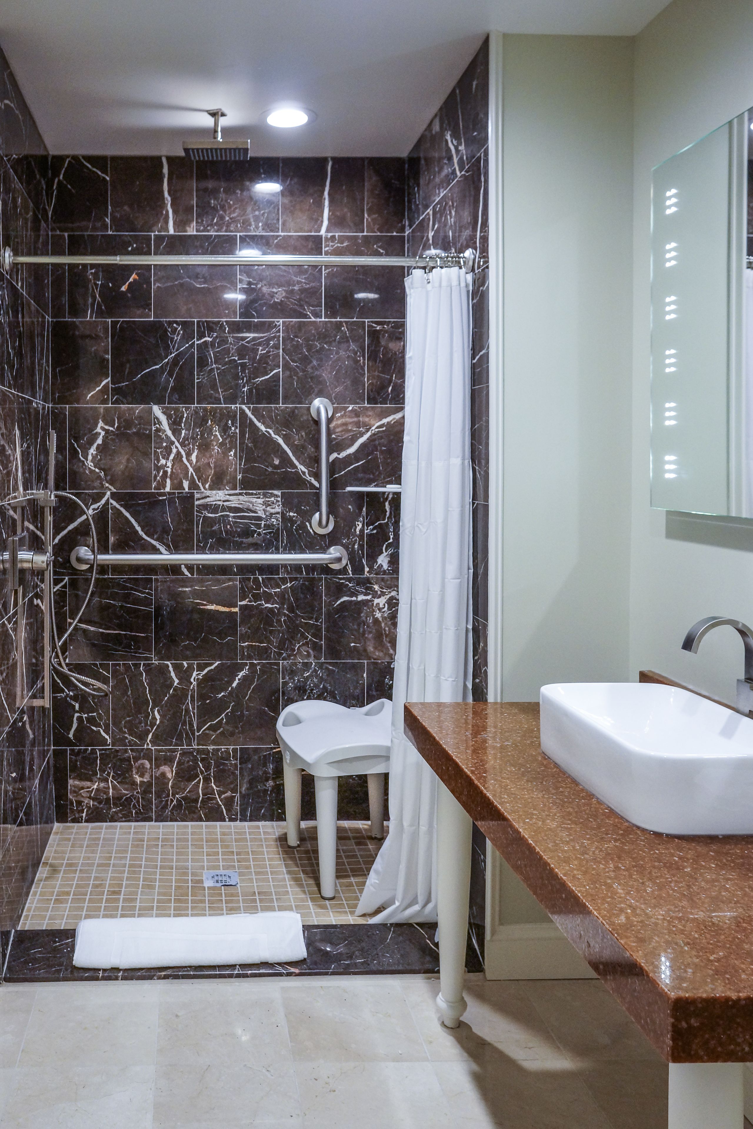 Une salle de bain moderne avec un mur de douche en marbre, un lavabo blanc et une paroi de douche en verre.
