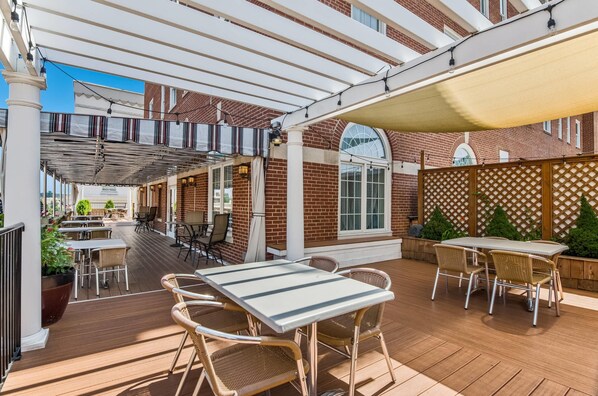 An outdoor patio area with wooden flooring, wicker furniture, and a covered seating area. - The Gin Hotel, an Ascend Collection Hotel (Lexington)