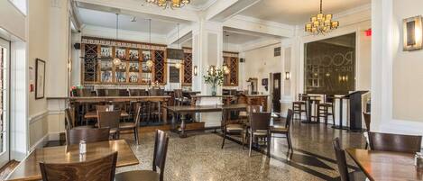 Un restaurante espacioso con techos altos, candelabros y una zona de bar con estantes llenos de botellas.