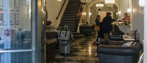 A hotel lobby with a checkered floor, a staircase, and a reception desk.