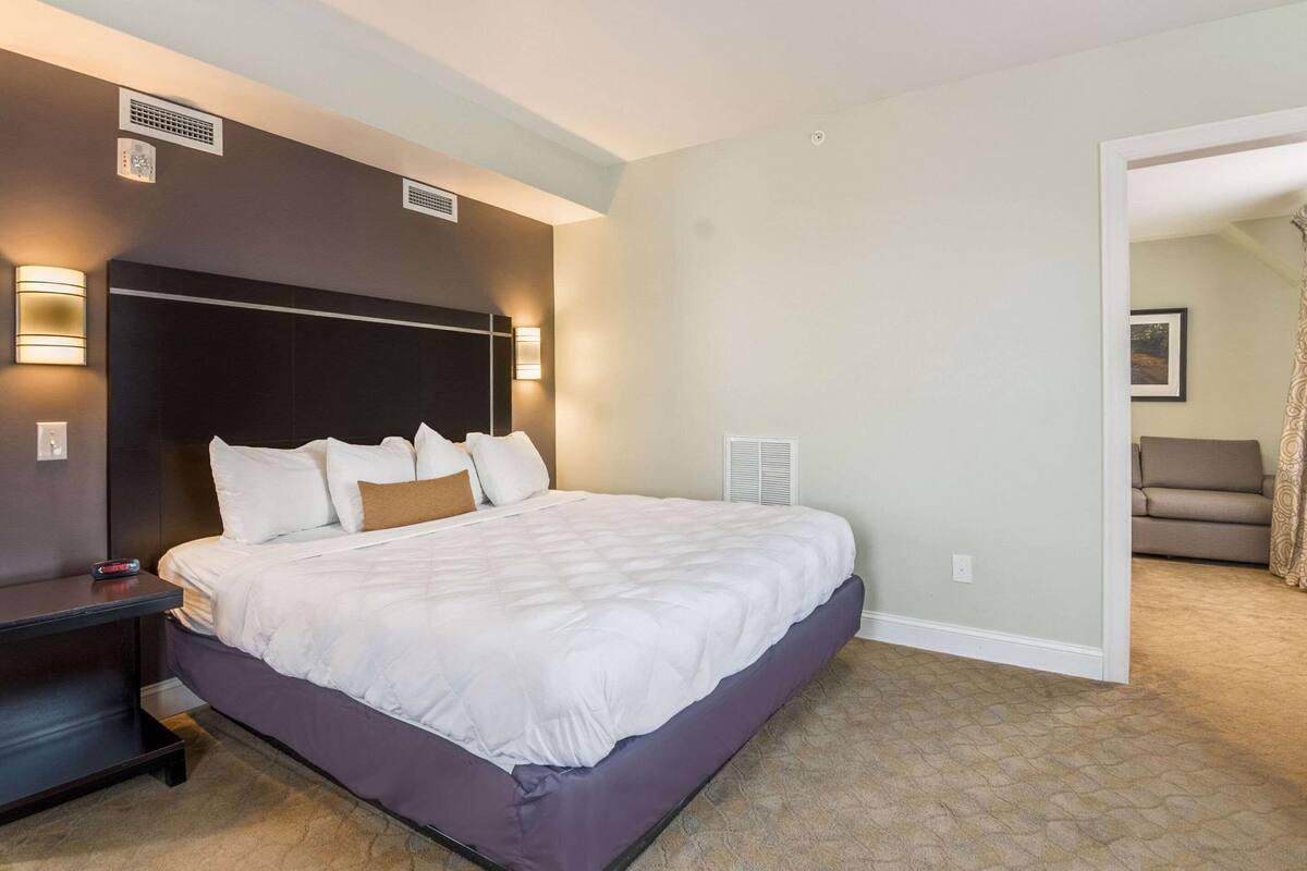 A hotel room with a large bed, bedside tables, wall-mounted lights, a thermostat, and a view of the hallway.