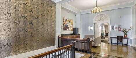Un vestíbulo amplio con una escalera, un candelabro y una obra de arte moderno en la pared.