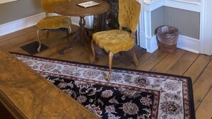 A dining area with a wooden table and two chairs, a fireplace with a mirror above, and a patterned rug on the floor.