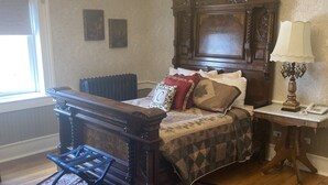 A traditional bedroom with a large wooden bed, a chandelier, a radiator, and a classic wooden nightstand.