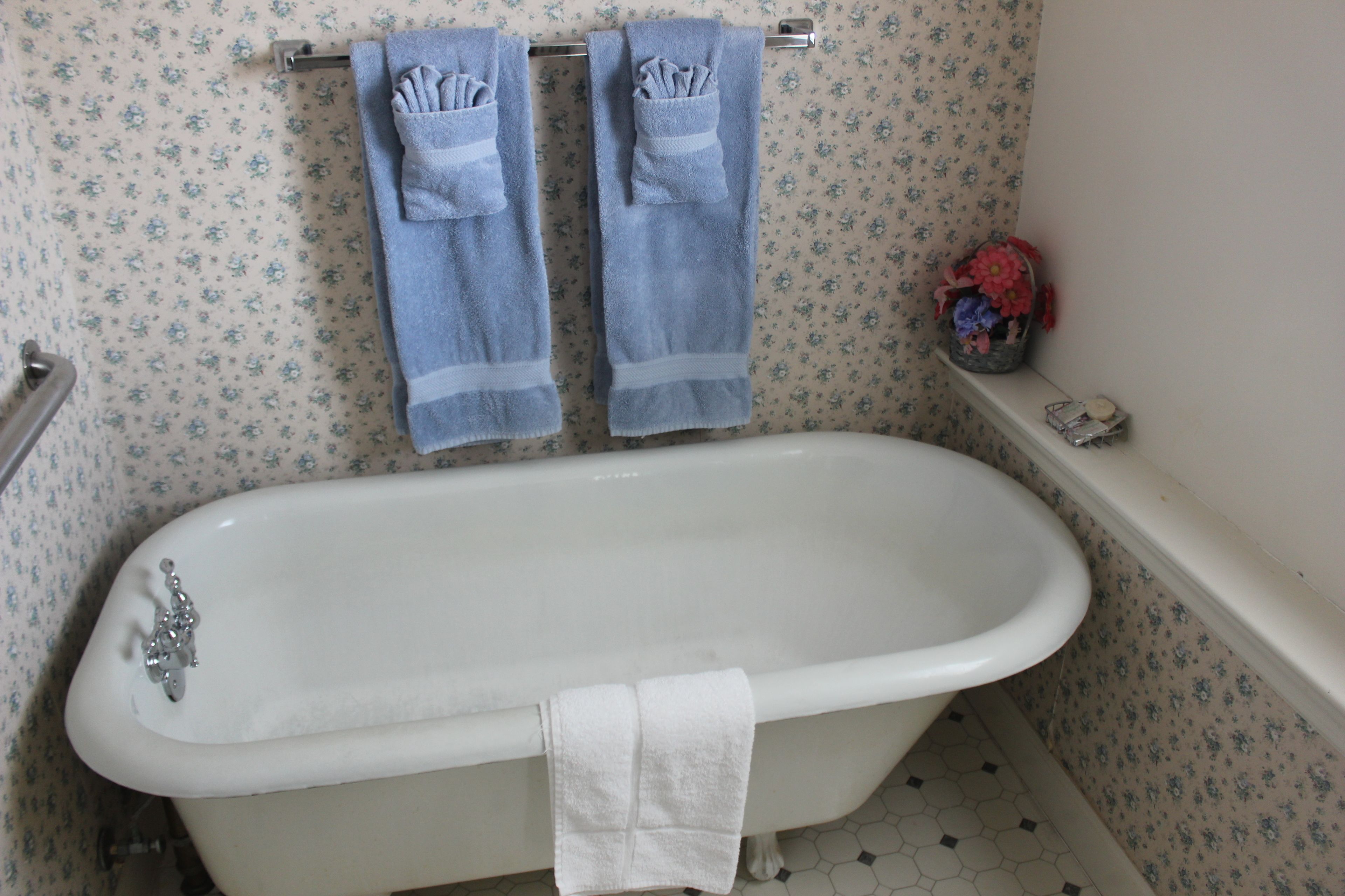 A bathroom with a white bathtub, two towels hanging on a towel rack, and a floral-patterned wall.