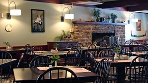 A restaurant with multiple tables and chairs, a stone fireplace, and wall-mounted lighting.