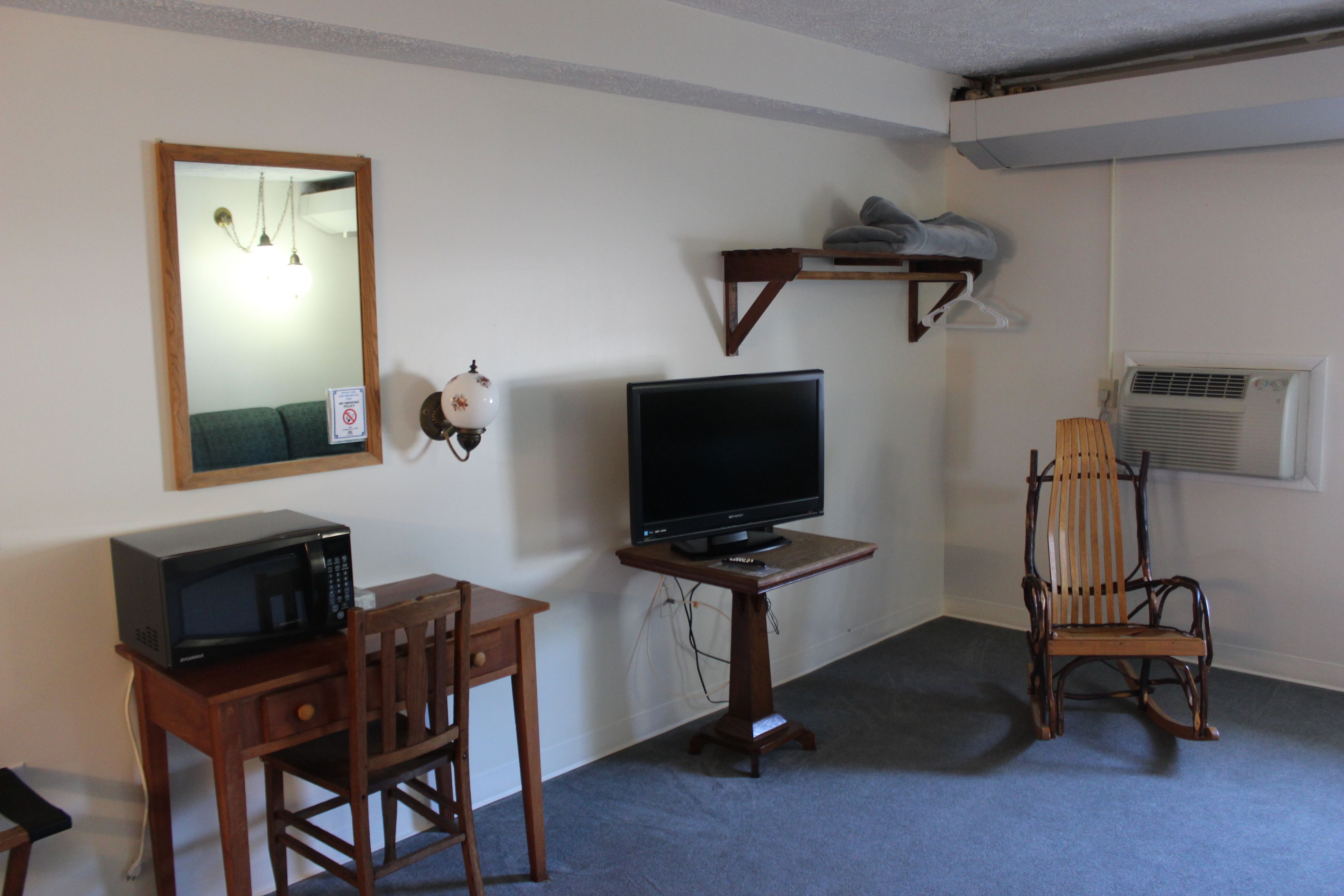 A room with a wooden desk, a television, a chair, a mirror, and a shelf with towels.