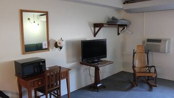 A room with a wooden desk, a television, a chair, a mirror, and a shelf with towels.