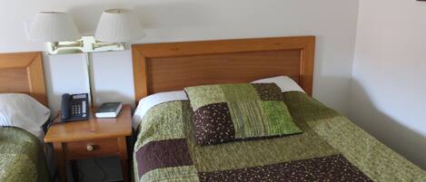 A hotel room with a wooden headboard, a bedside table with a lamp, a telephone, and a quilted bedspread.