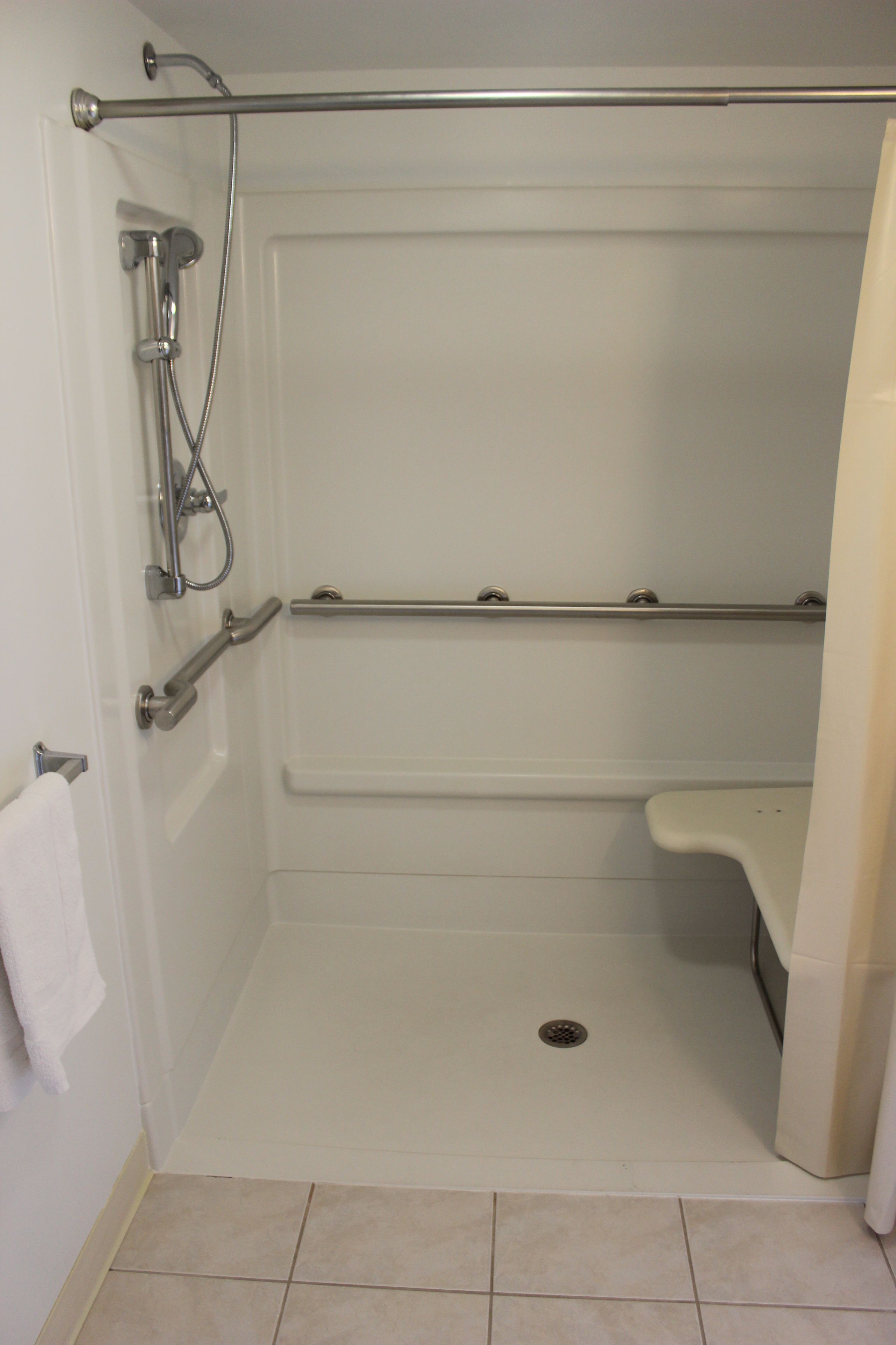 A shower with a grab bar, a white toilet, and a white sink.