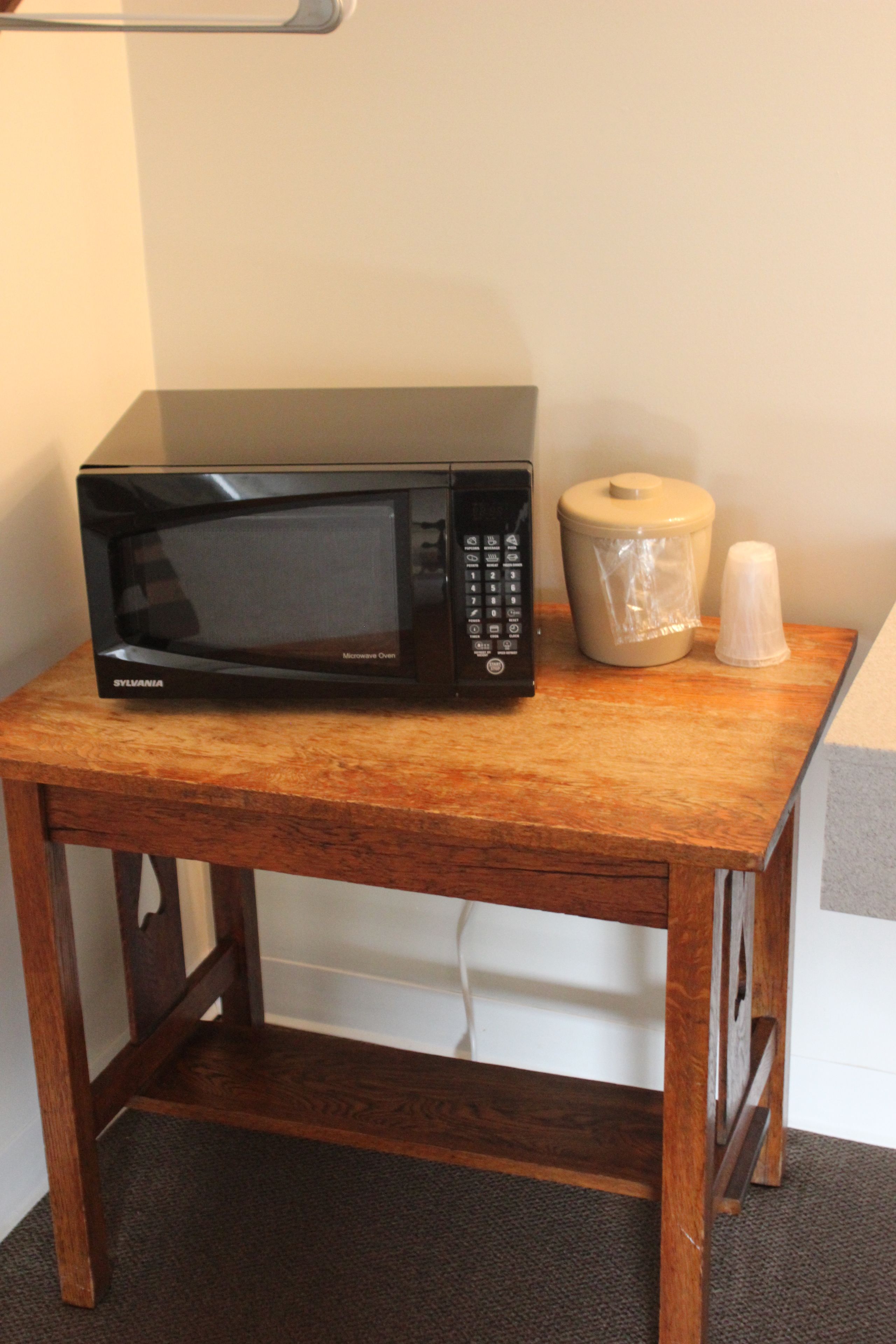 Un four à micro-ondes posé sur une table en bois, avec un récipient en plastique et un gobelet en plastique.