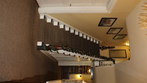 A staircase with a white railing, a wooden handrail, and a carpeted floor. There are framed pictures on the wall and a Christmas garland above the staircase.