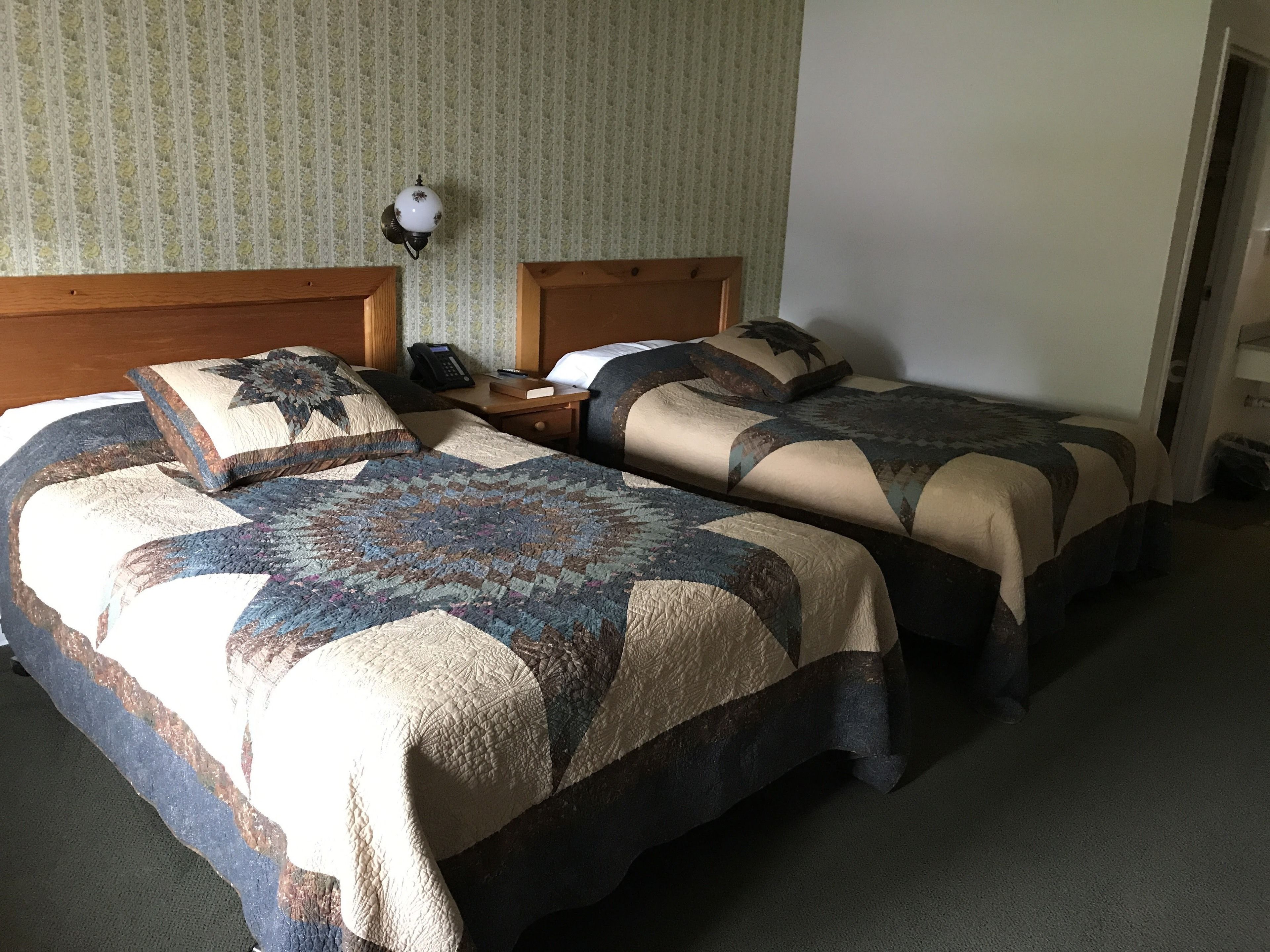 Habitación de hotel con dos camas, una mesita de noche, un teléfono y una lámpara fijada a la pared.
