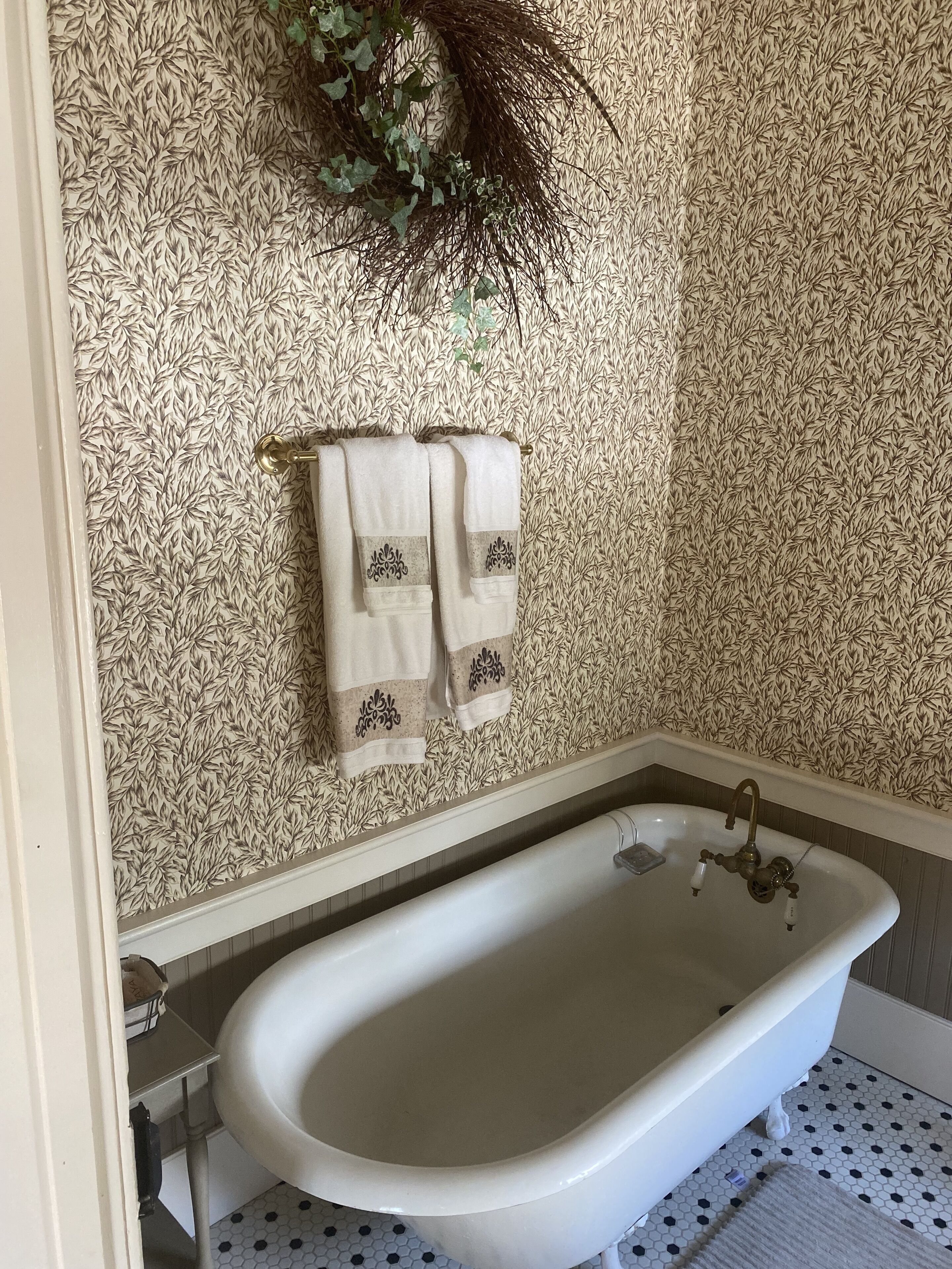 A bathroom with a white bathtub, a towel rack with two towels, and a patterned wallpaper.