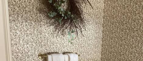 Un baño con una bañera blanca, un perchero con dos toallas y un papel tapiz estampado.