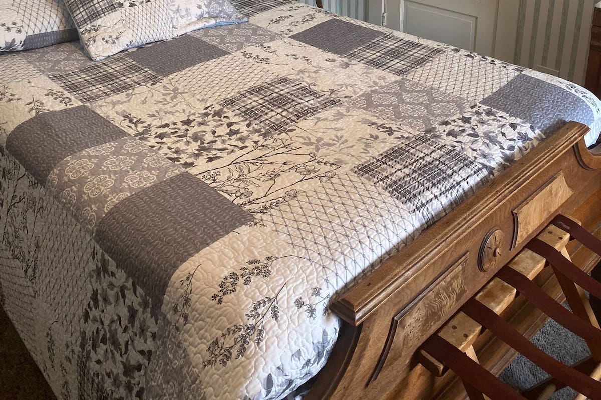 Una cama con colcha, una mesita de noche con lámpara y una puerta en una habitación con papel tapiz a rayas.