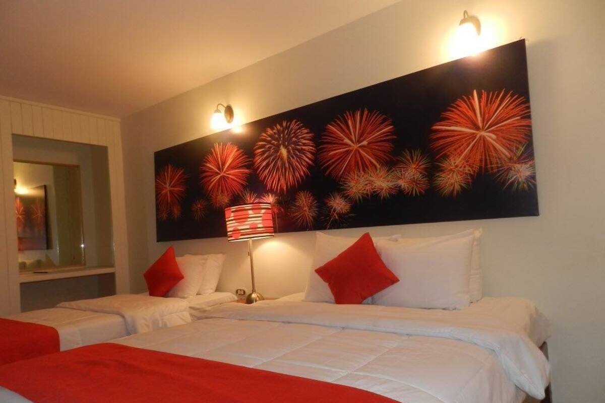 A hotel room with two beds, a large wall mural of fireworks, and a bedside lamp.