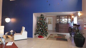 A living room with a white sofa, a Christmas tree, a clock on the wall, and a kitchen area in the background. - Green Palm Boutique Hotel (Crown Point)