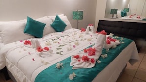 A neatly made bed with a teal bedspread, white pillows, and a floral arrangement on the bed. - Green Palm Boutique Hotel (Crown Point)