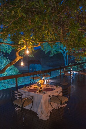 An outdoor dining area with tables and chairs under a tree, surrounded by a wooden deck and a railing. - Waterbuck Game Lodge (Bushbuckridge)