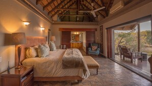 Une chambre spacieuse avec un grand lit, un plafond en bois et une vue sur la cuisine et l’espace extérieur.