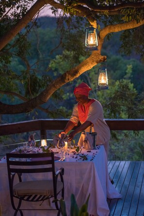 A table set outdoors with a person preparing food, surrounded by lanterns and a natural backdrop. - Waterbuck Game Lodge (Bushbuckridge)