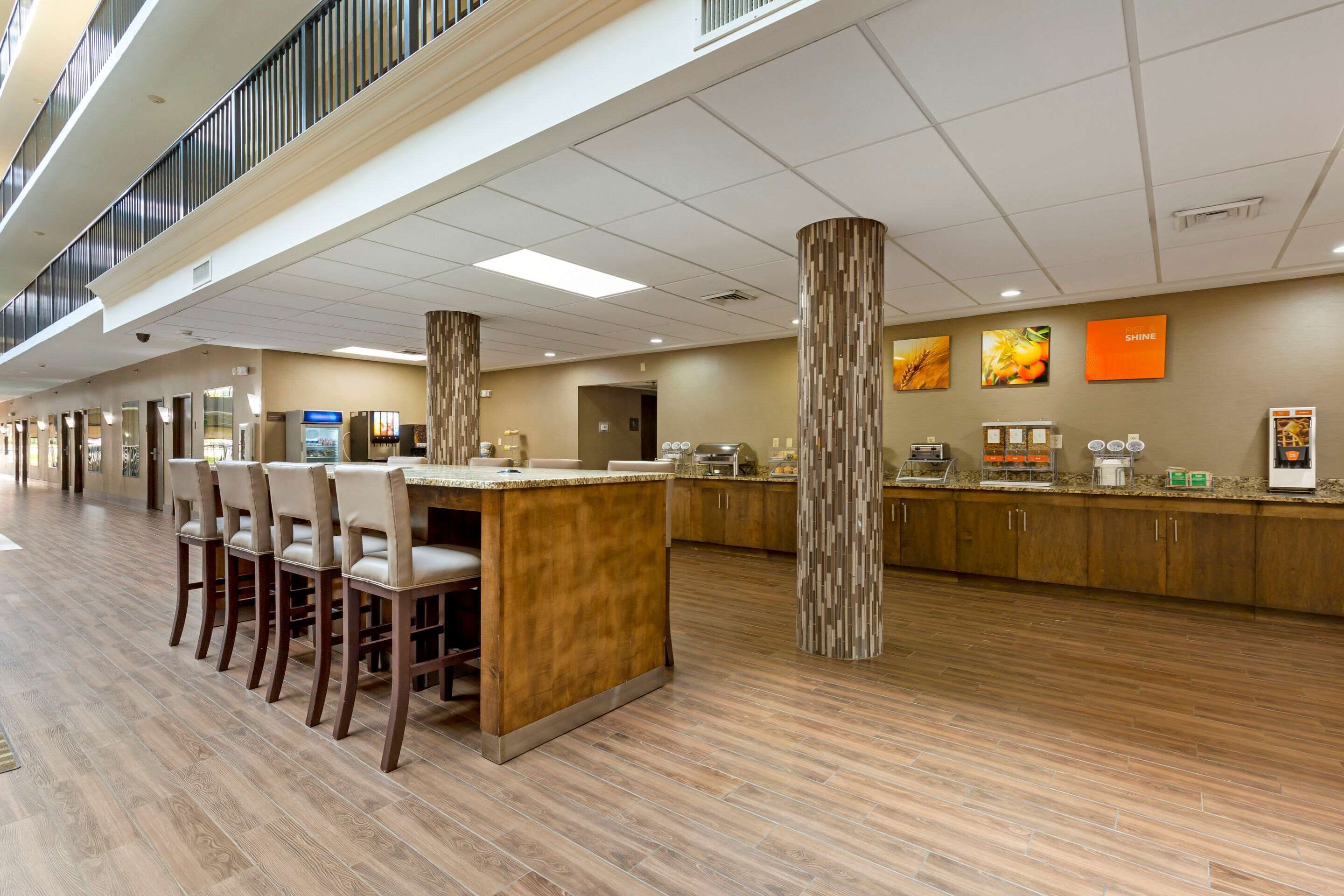 A spacious hotel lobby with a long reception desk, multiple chairs, and a high ceiling with a grid pattern.