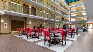 Un hall de hotel de varios niveles con zonas de comedor, piscina y un techo alto con tragaluces.