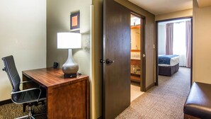 Una habitación de hotel con escritorio, silla, lámpara y cama con manta azul.