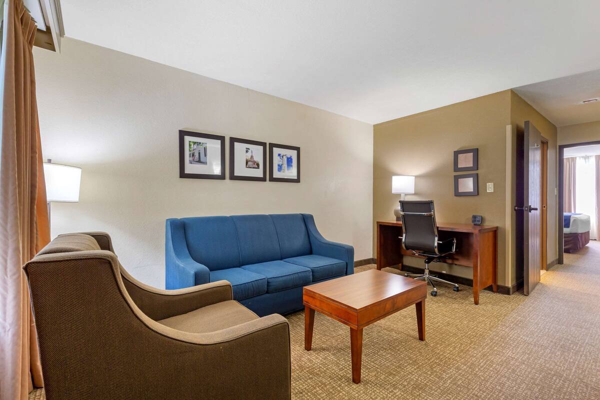 Habitación de hotel con sofá azul, una mesita de madera, escritorio con silla y cuadros en la pared.