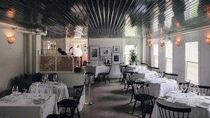 A restaurant with multiple tables set for dining, a bar area, and framed artwork on the walls. - The Maidstone (East Hampton)