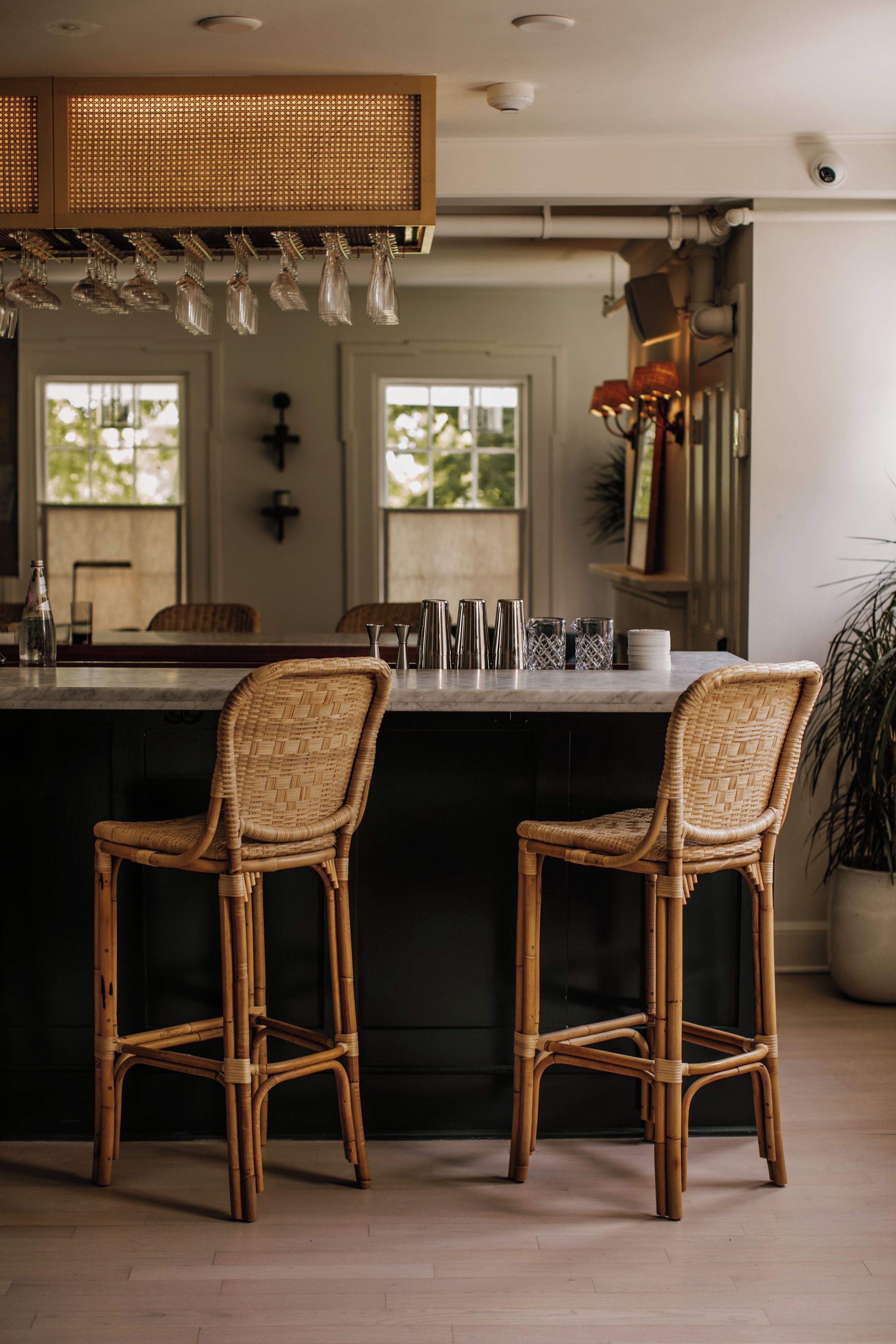 A kitchen with a central island, two wicker chairs, and a bar area with glasses.