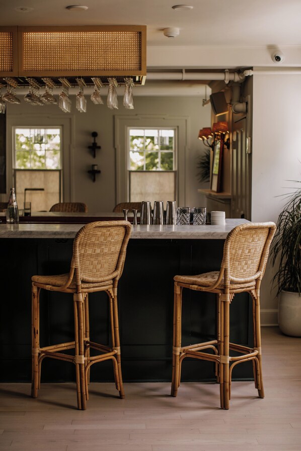 Una cocina con una isla central, dos sillas de mimbre y una zona de bar con vasos.