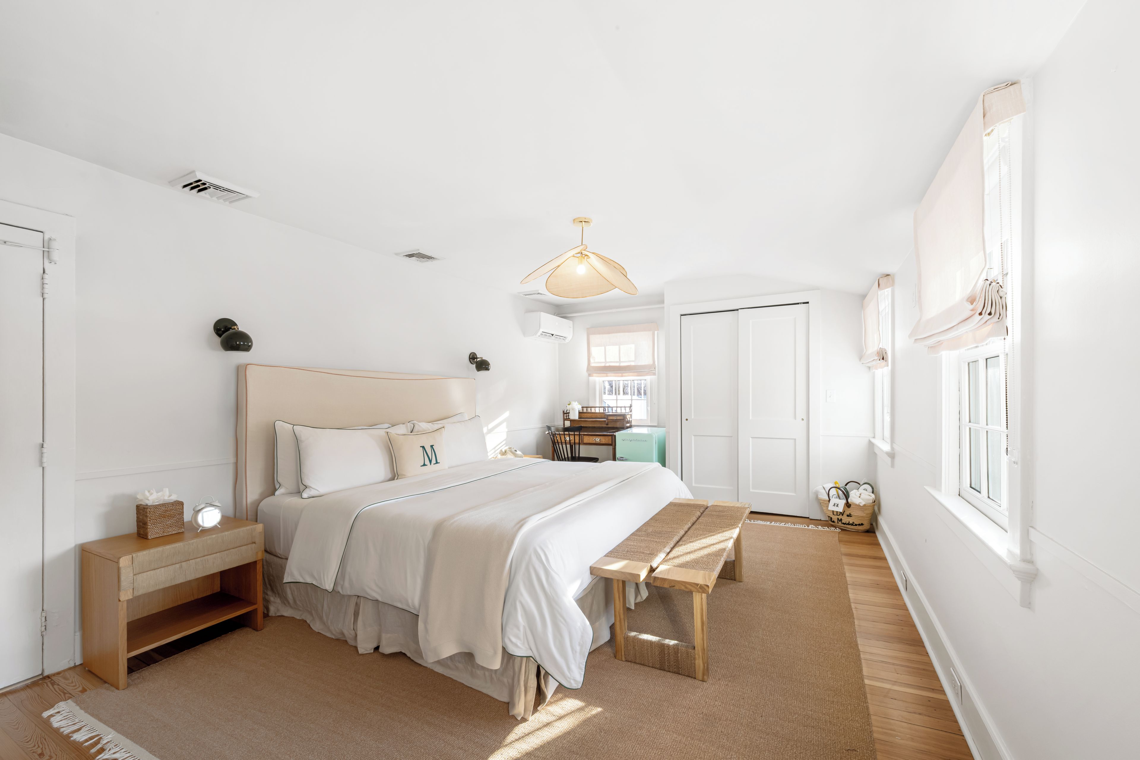 A bedroom with a large bed, bedside tables, a bench, a desk, and a window.