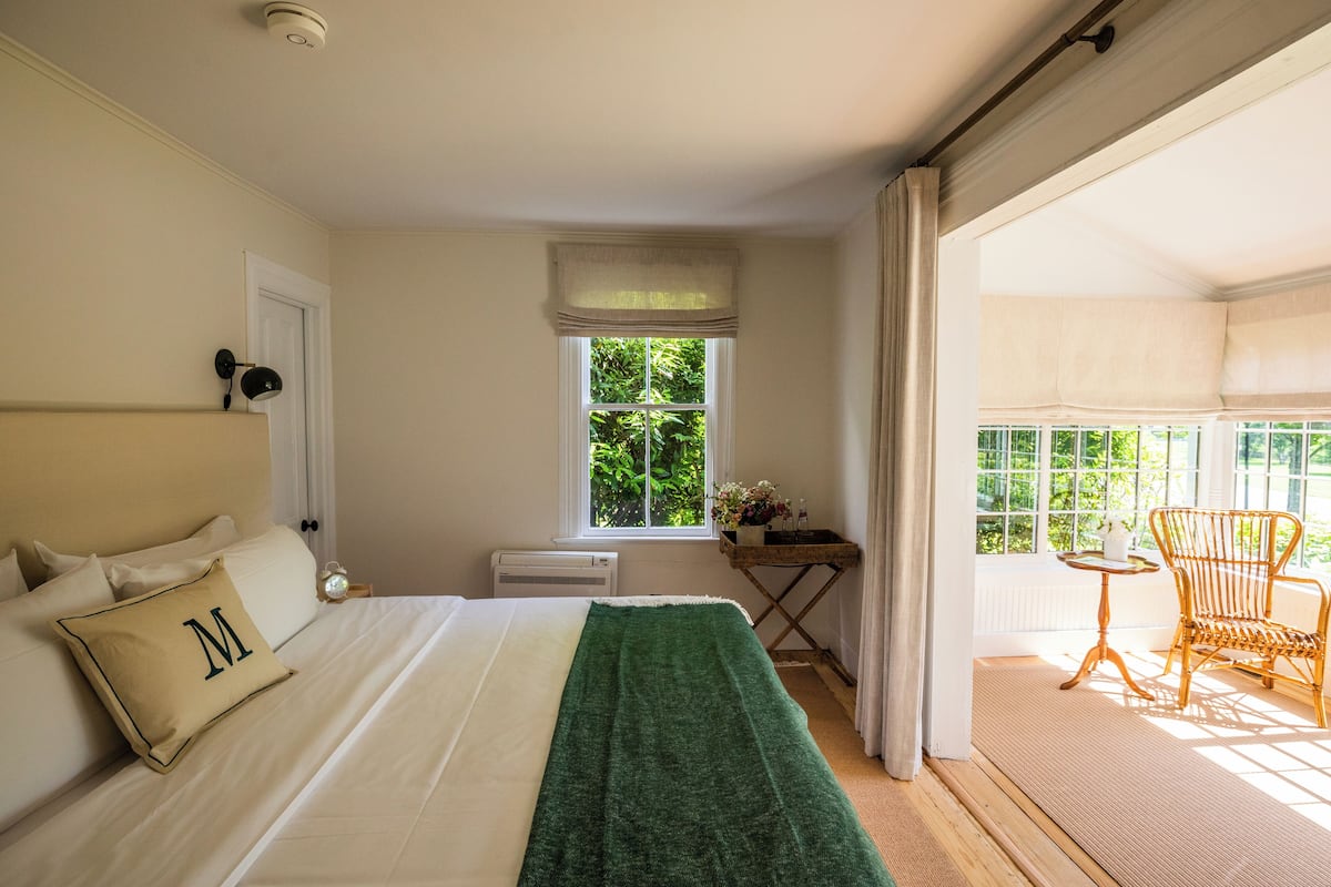 A bedroom with a bed, a window, a chair, and a small table with a vase.
