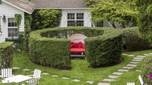 Une maison blanche avec une porte rouge, entourée d’un jardin bien entretenu, agrémenté de haies et d’un chemin en pierre.