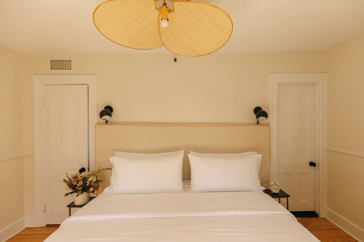 A bedroom with a large bed, two bedside tables, a ceiling fan, and a wall-mounted clock.