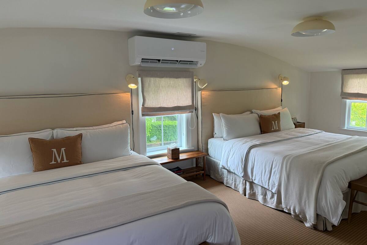 A hotel room with two beds, a large window, and an air conditioning unit.